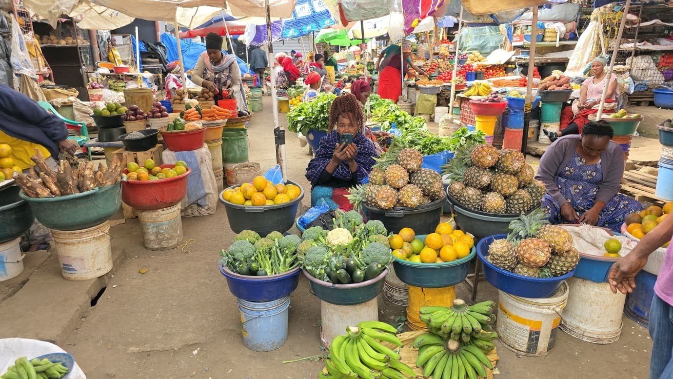 Traders seated among basins of pineapples, oranges, bananas and greens in the central market at Arusha