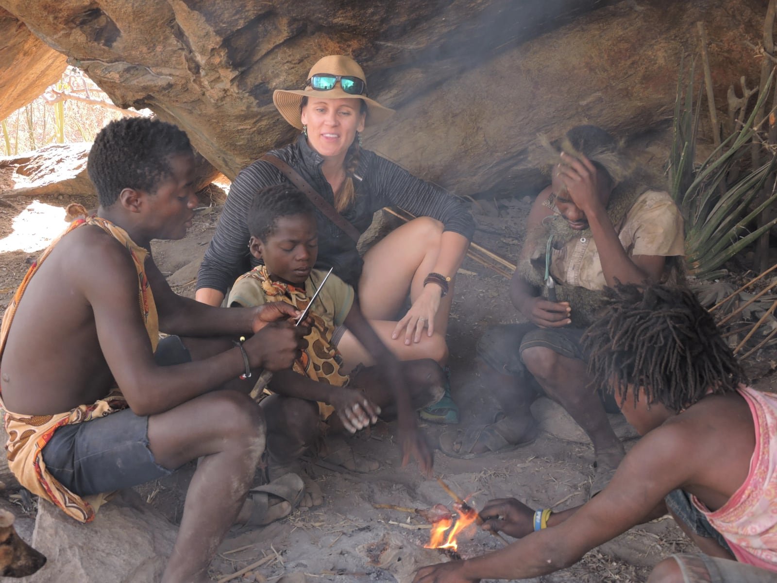 A guest with Hadzabe hunters sharing fire and roasted meat in a rock shelter