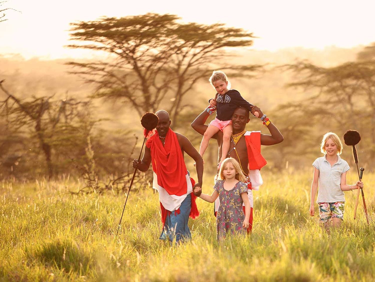 Maasai guides walking through the grass with children on a family safari