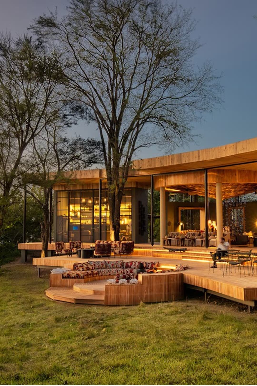 The lit deck and glass-walled bar at Grumeti River Lodge at dusk, West Serengeti